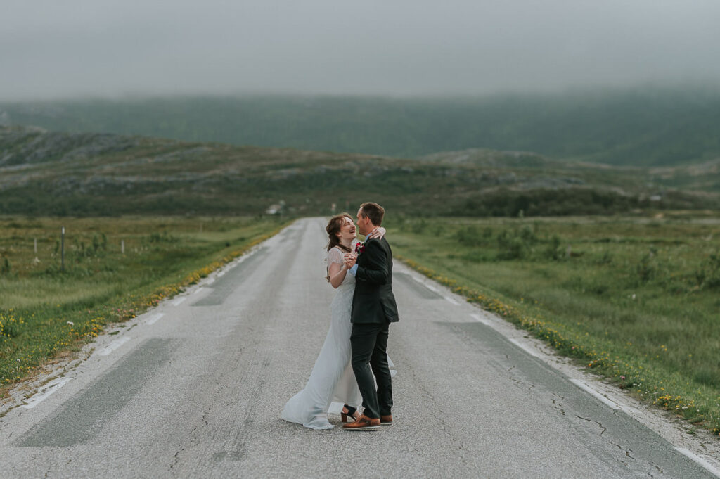 Bride and groom dancing and laughing in the middle of an empty road in front of clody mountain landscape