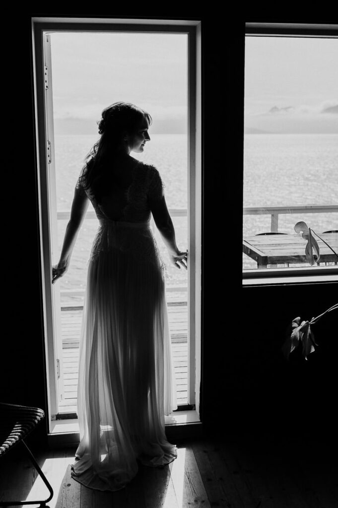 Black and white portrait of the bride standing in front of the balcony window