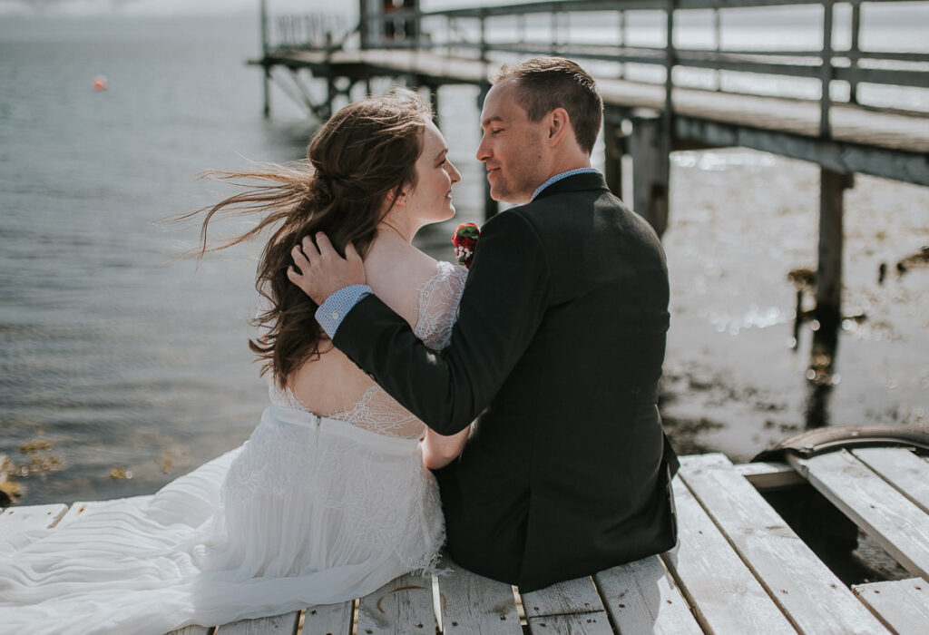 Bride and groom sitting on an old wooden pier and hugging on a nice summer day