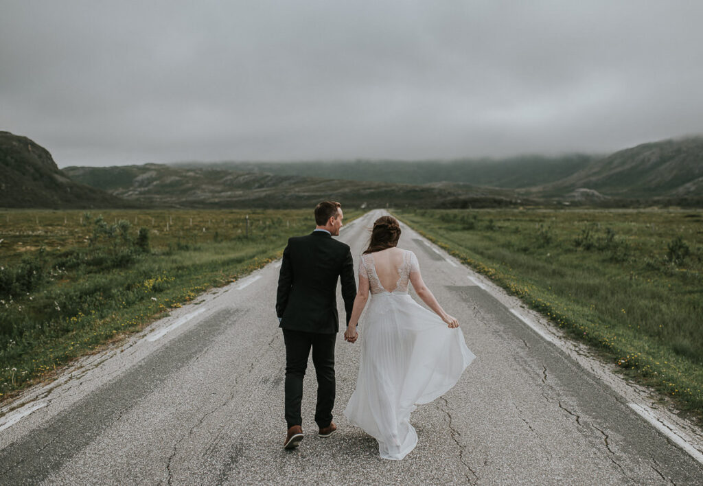 Bride and groom walking in the middle of the road towards beautiful mountains 