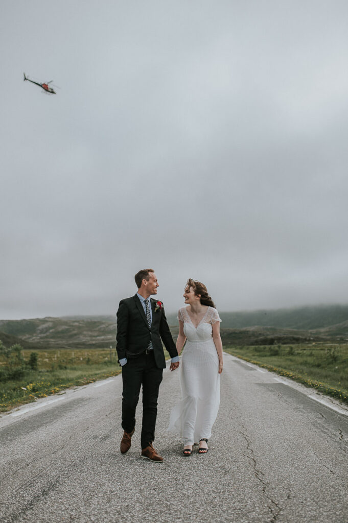 Bride and groom walking in the middle of the road while helicopter is flying above them