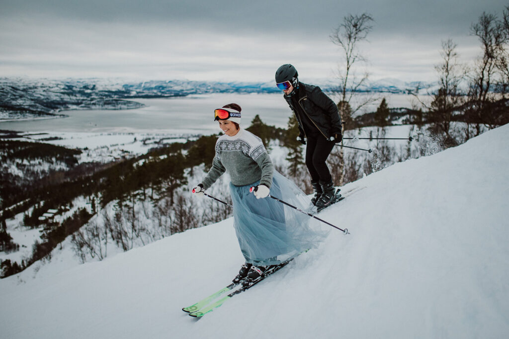 Cute couple in wedding attire slalom skiing down the hills on the day of their winter elopement in Alta Norway