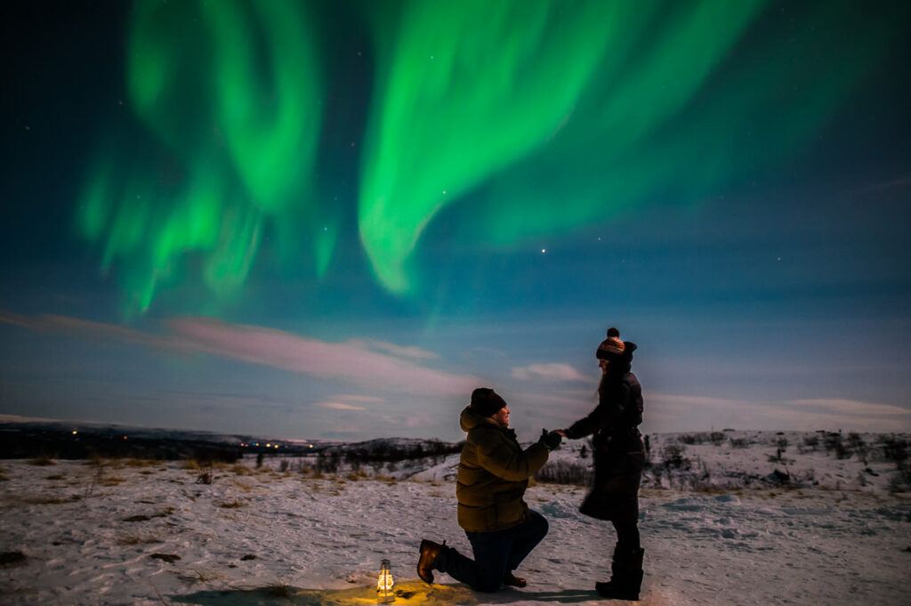 Proposal under the northern lights - a guy stands on his knee and asks his girlfriend to marry him under beautiful northern lights in Alta Norway