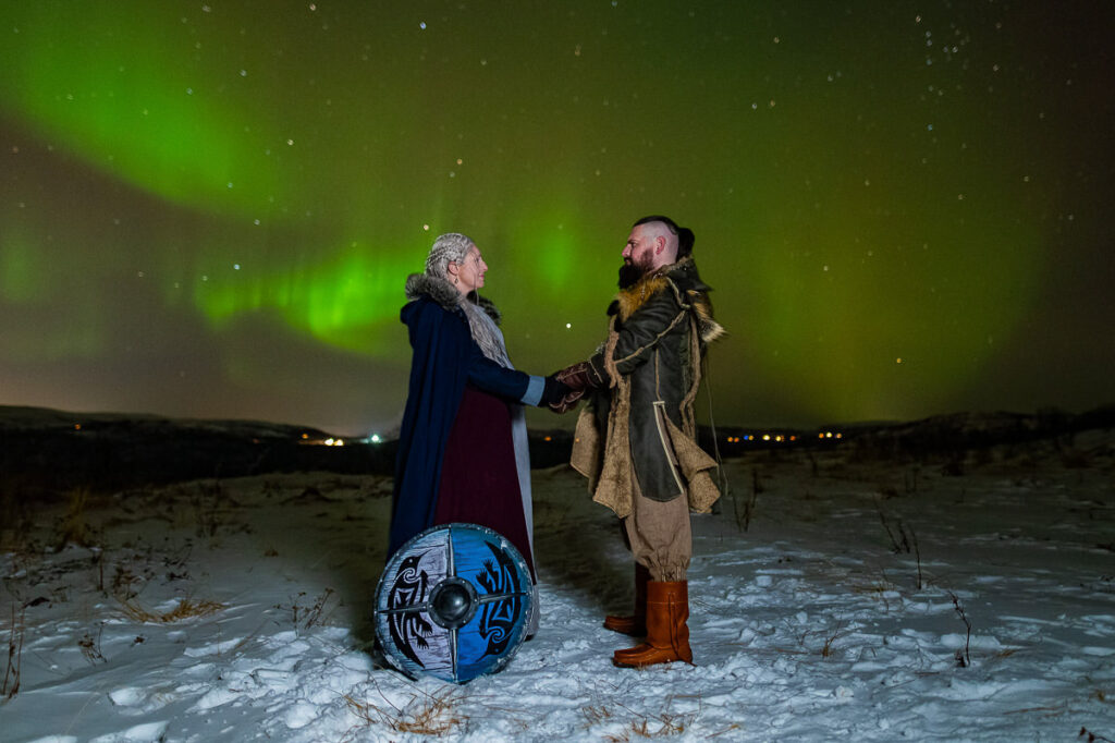 Viking shieldmaiden and viking king holding hands under the northern lights in Northern Norway