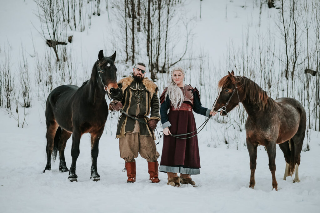 Viking couple in leather armor walking around with two horses in front of a snowy landscape in Alta Norway
