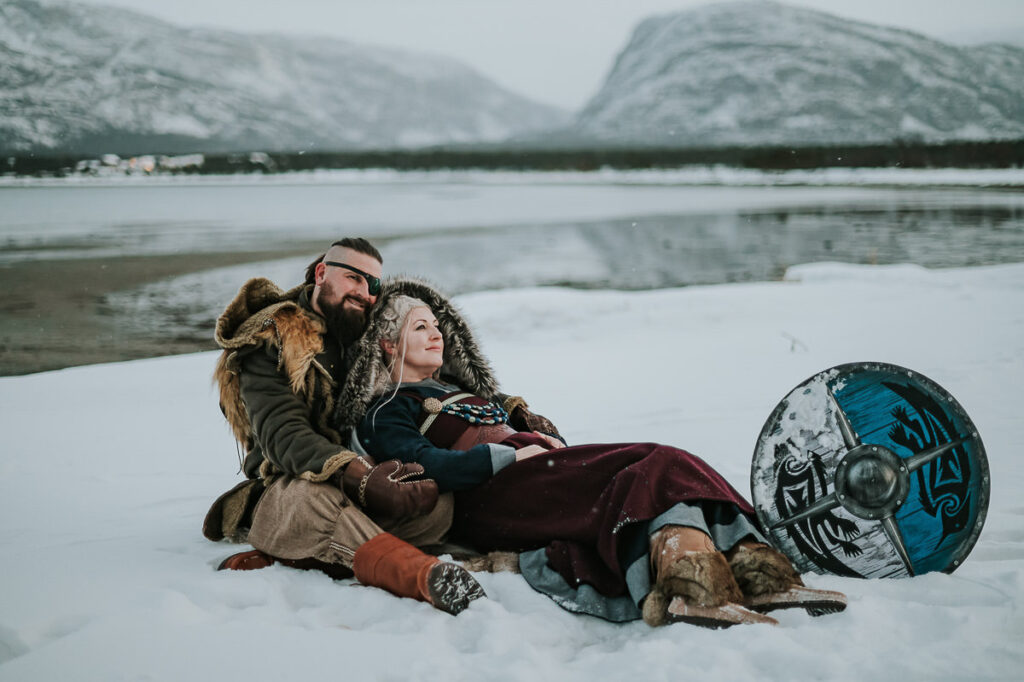 Viking couple sitting in the snow in front of a beautiful winter landscape with mountains and fjords in Alta Norway
