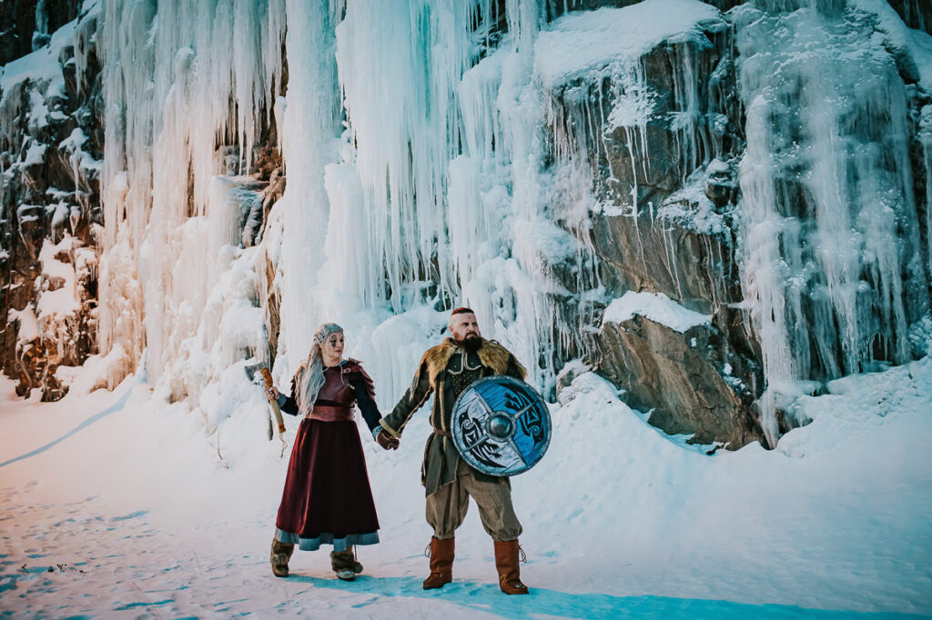 Viking style elopement portraits where the couple is posing in front of gorgeous frozen waterfalls in Northern Norway