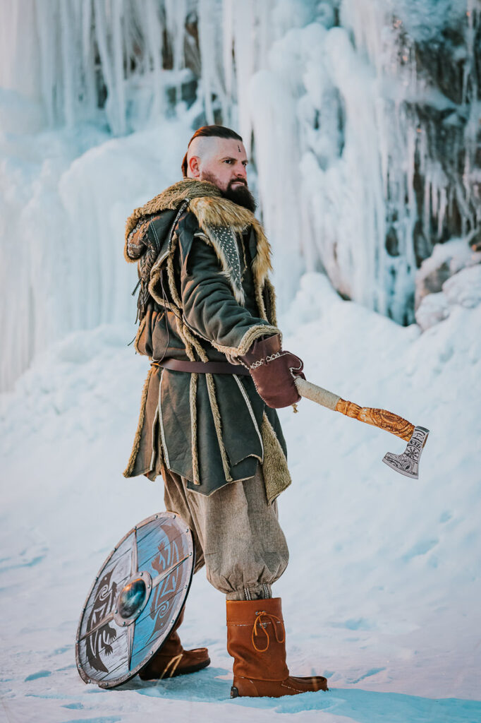 Male viking in a cool fur outfit posing in front of a frozen waterfall in Norway
