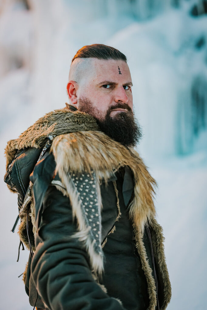 Male viking in a cool fur outfit posing in front of a frozen waterfall in Norway