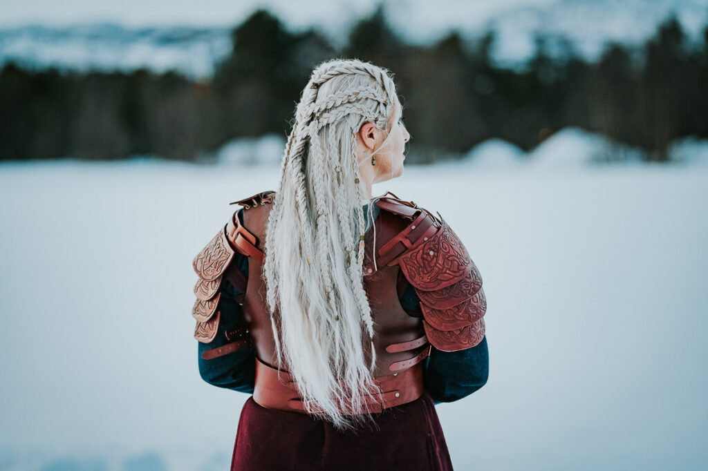 Viking shieldmaiden showing off her beautiful blond hair with viking style  braids. She is standing in front of a winter snowy landscape in Norway