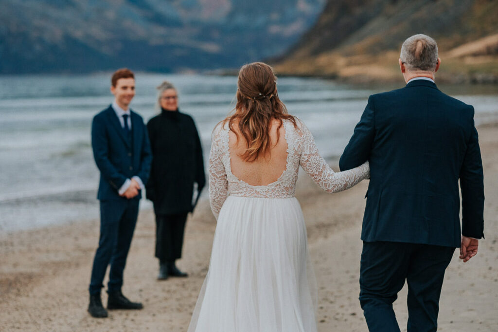Intimate wedding ceremony on a beach near Tromsø in Norway. Bride and her father walking towards the groom and the celebrant