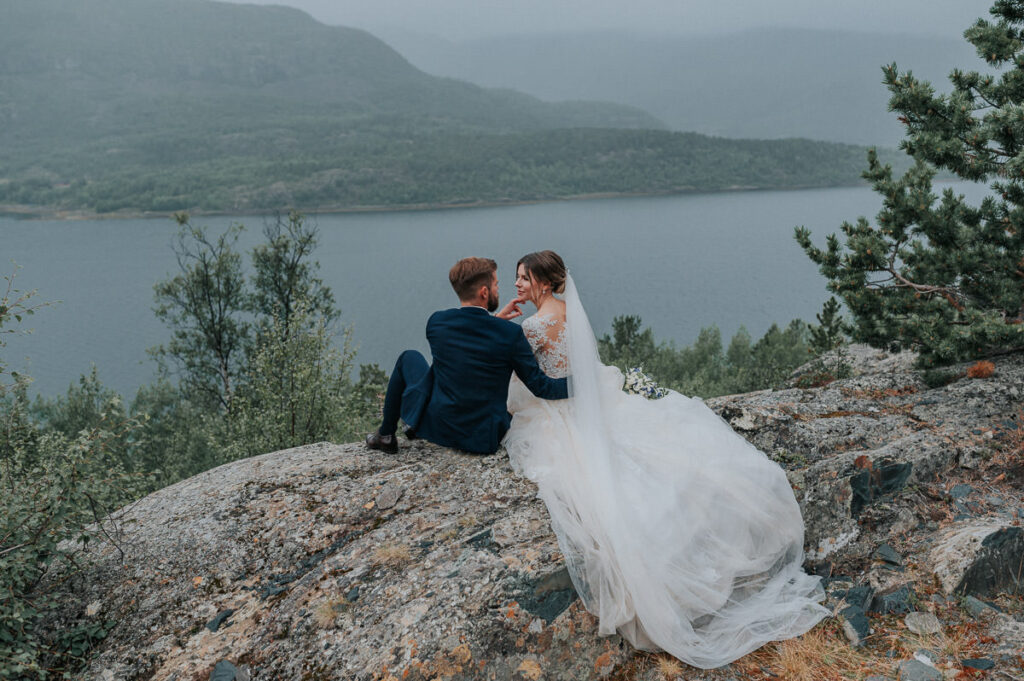 Nydelig brudepar sitter på bergene i regnværet med fjord og fjell utsikt - beste foto locations for et bryllup i Alta