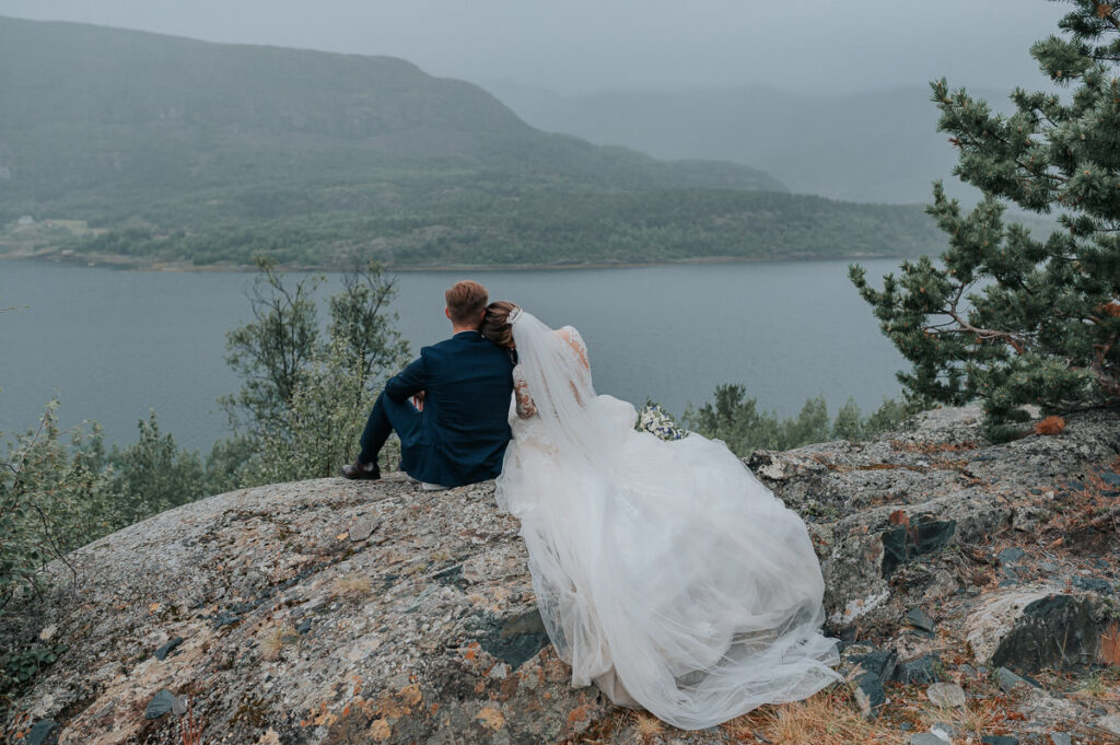 Nydelig brudepar sitter på bergene i regnværet med fjord og fjell utsikt - beste foto locations for et bryllup i Alta