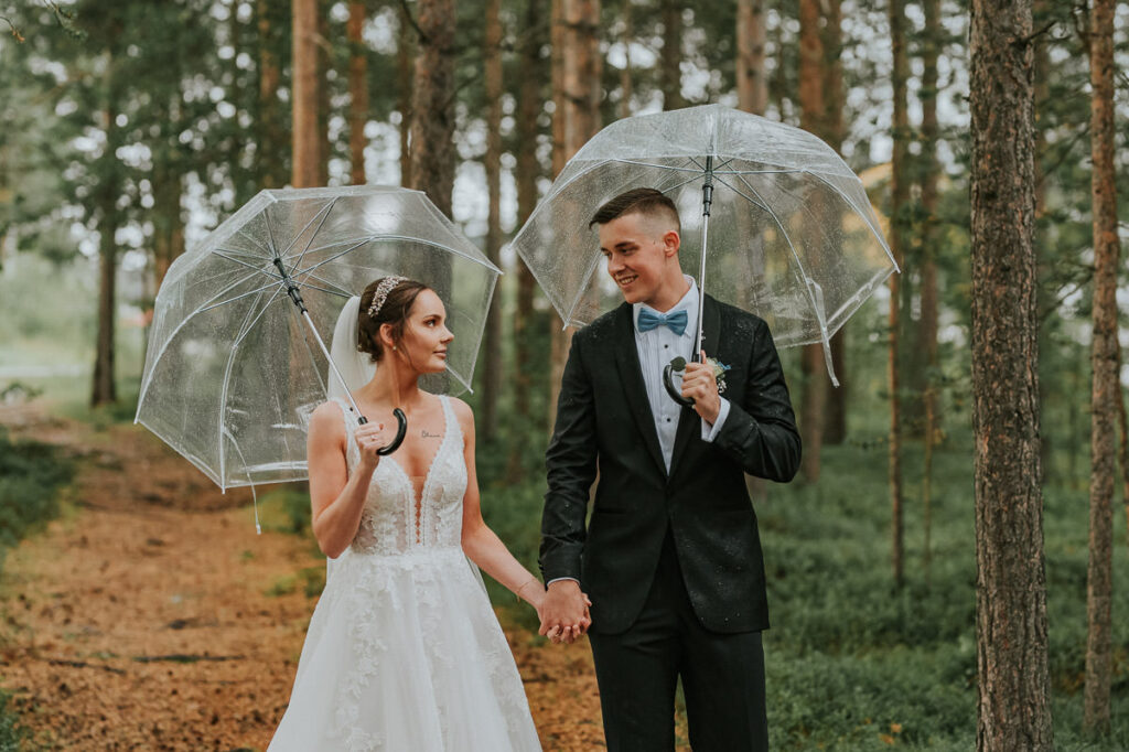 Nydelig brudepar under blanke paraplyer i en skog på en regnværsdag i Alta
