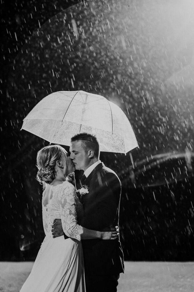Svart hvit portrett bilde av et brudepar som kysser under paraply på en regnværsdag i Alta