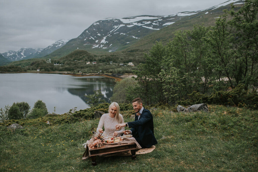 Vakkert brudepar spiser picnic foran et vakkert utsikt til fjord og fjell i Alta Norge - beste foto locations for et bryllup