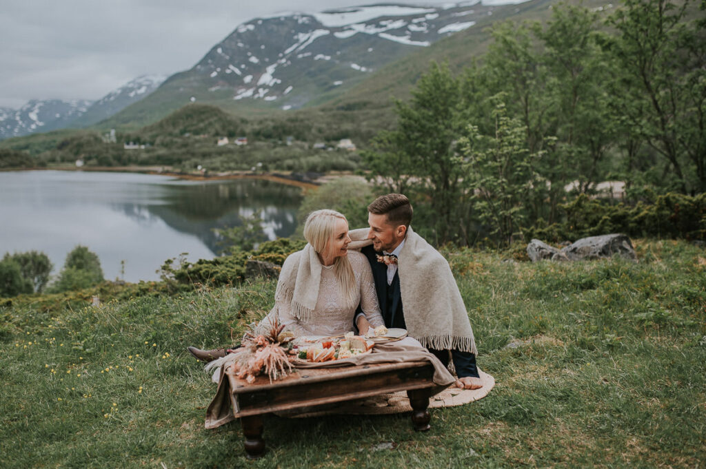 Vakkert brudepar spiser picnic foran et vakkert utsikt til fjord og fjell