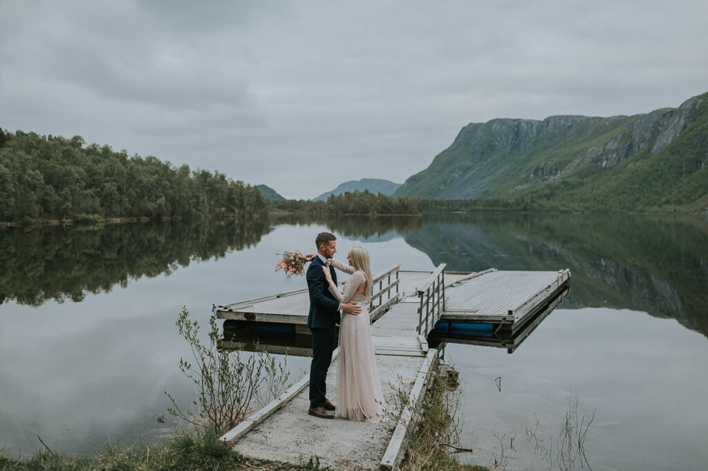 Brudepar står på brygga foran et innsjø og fjell i Alta, Finnmark