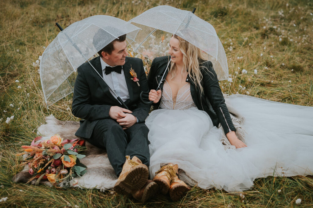 Brudepar sitter i et gyldent åker under paraplyene på en regnfull bryllupsdag