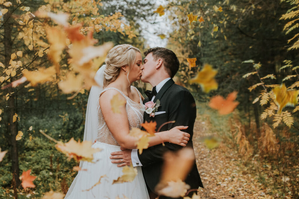 Nydelig brudepar kysser i en høstkledd skog mens fargerike bladene faller på dem - beste foto locations for bryllup i Alta
