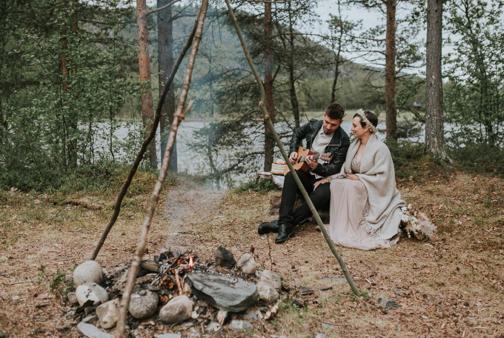 Nydelig brudepar sitter foran bålet og spiller gitar