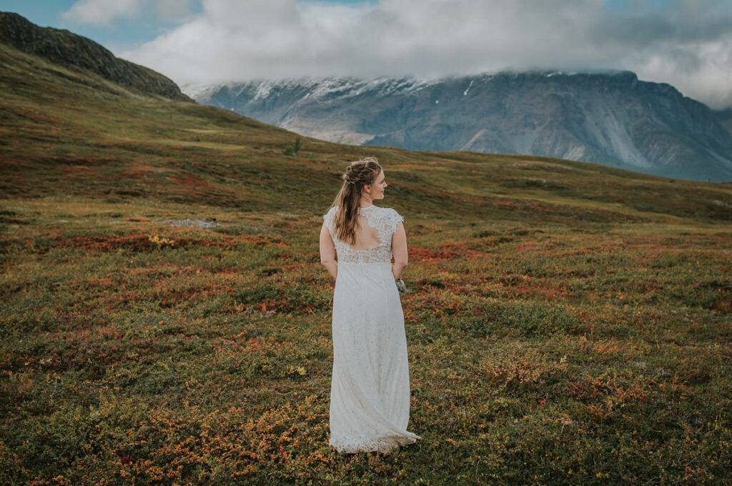 Nydelig brud i en blonderkjole med en åpen rygg foran et vakkert fjelllandskap på en høstdag i Alta