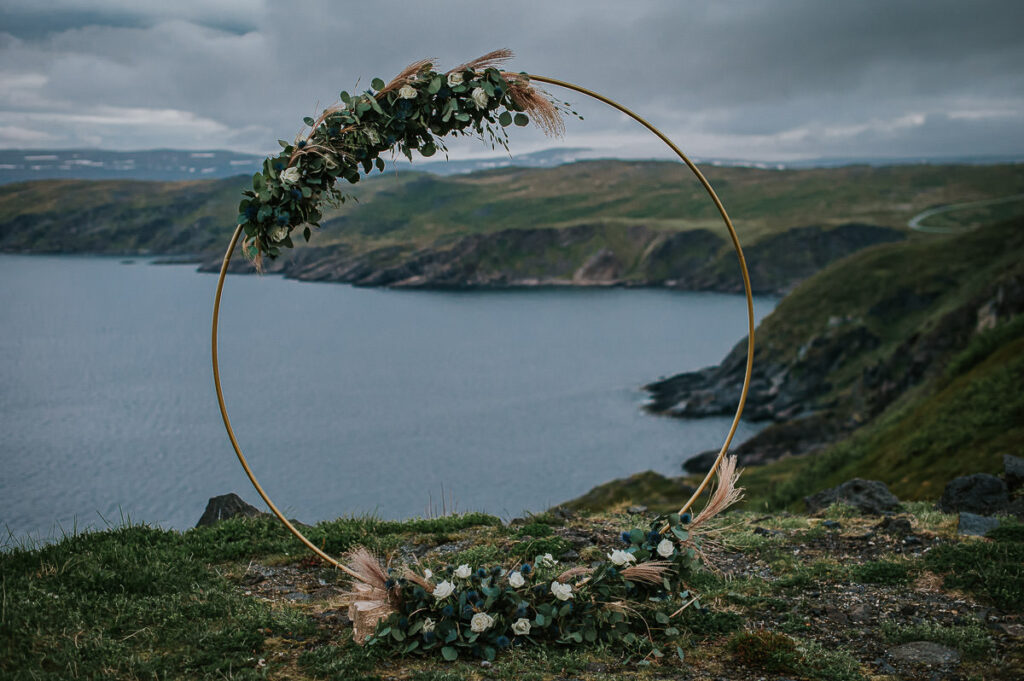 Round floral arch standing in front of a beautiful nordic landscape in Norway. The arch is decorated with blue and green flowers 