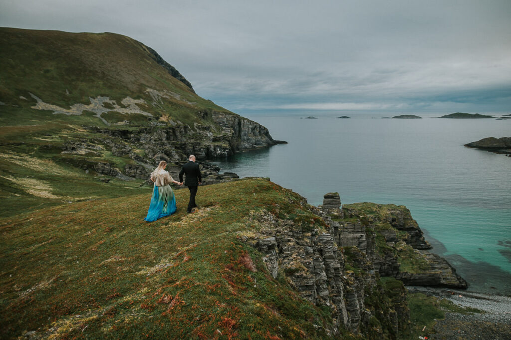 Bride and groom are walking among beautiful landscapes on Sørøya island in Northern Norway on the day of their midnight sun elopement 