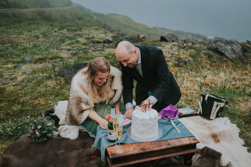 Bride and groom eating their wedding cake outdoors after their midnight sun elopement wedding ceremony on Sørøya