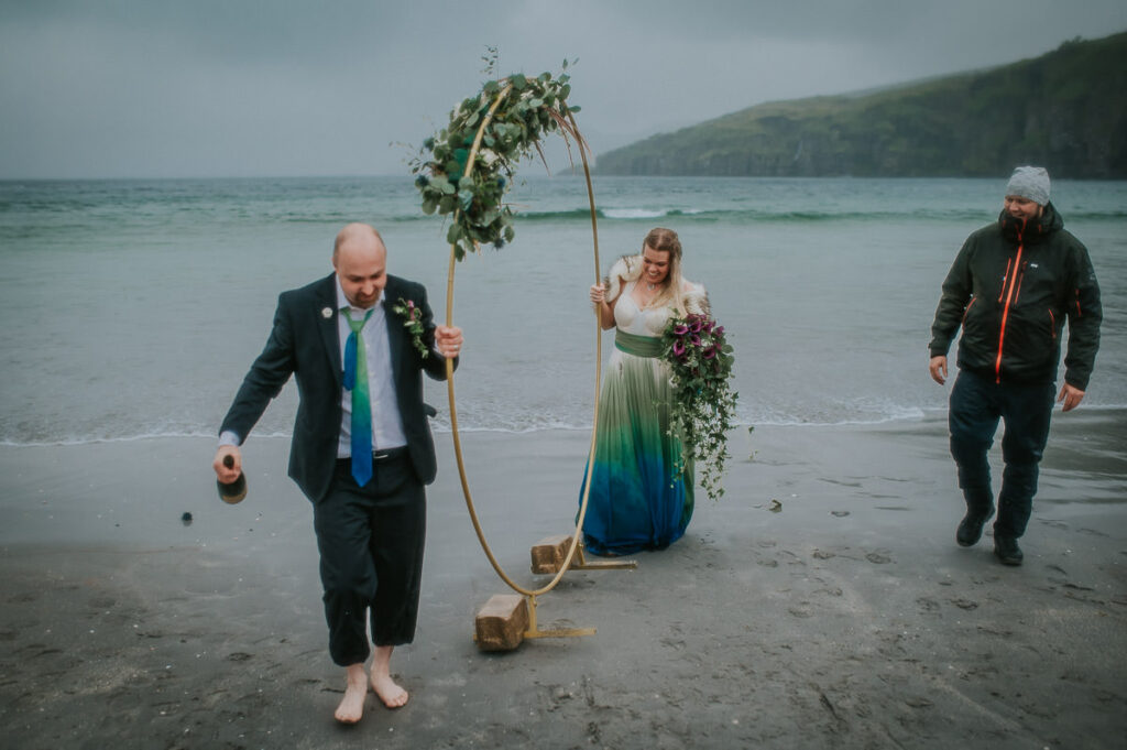 Bride and groom carrying their flower arch from the sea in Sørøya island in Northern Norway