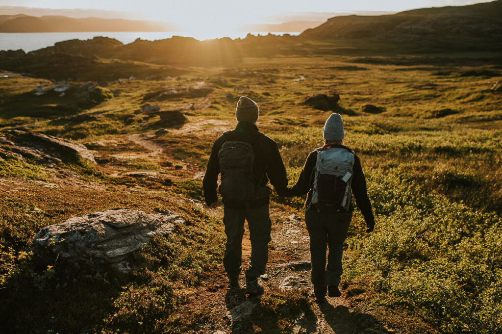 A couple with backpacks walking towards midnignt sun on Sørøya in Norway