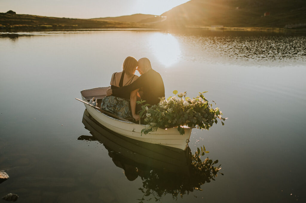 Beautiful couple rowing a boat on a lake in the midnight sun on Sørøya island in Norway - engagement photo session 
