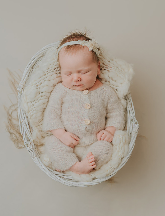 Vakker nyfødt jente i hvite strikket klær sover søtt i fotostudio på nyfødtfotografering hos TS Foto Design