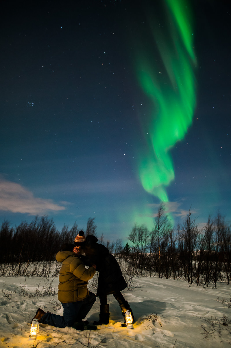 A guy on his knee propsing to his girlfriend under the northern lights in Alta Norway