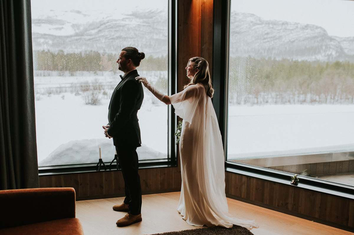 Bride and groom adjusted their elopement timeline due to heavy blizzard occuring on the day of their winter elopement. They are doing first look indoors in their luxury room at Sorrisniva wilderness Lodge in Alta Norway