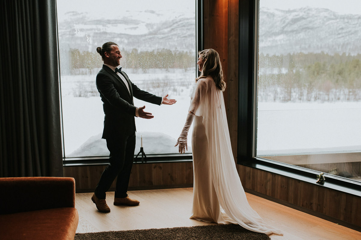 Bride and groom adjusted their elopement timeline due to heavy blizzard occuring on the day of their winter elopement. They are doing first look indoors in their luxury room at Sorrisniva wilderness Lodge in Alta Norway