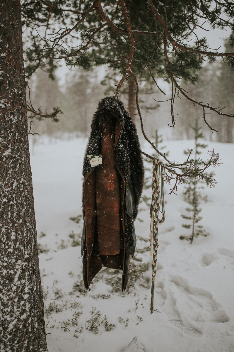 Male winter coat hanging on a tree in a forest under a snowfall. 