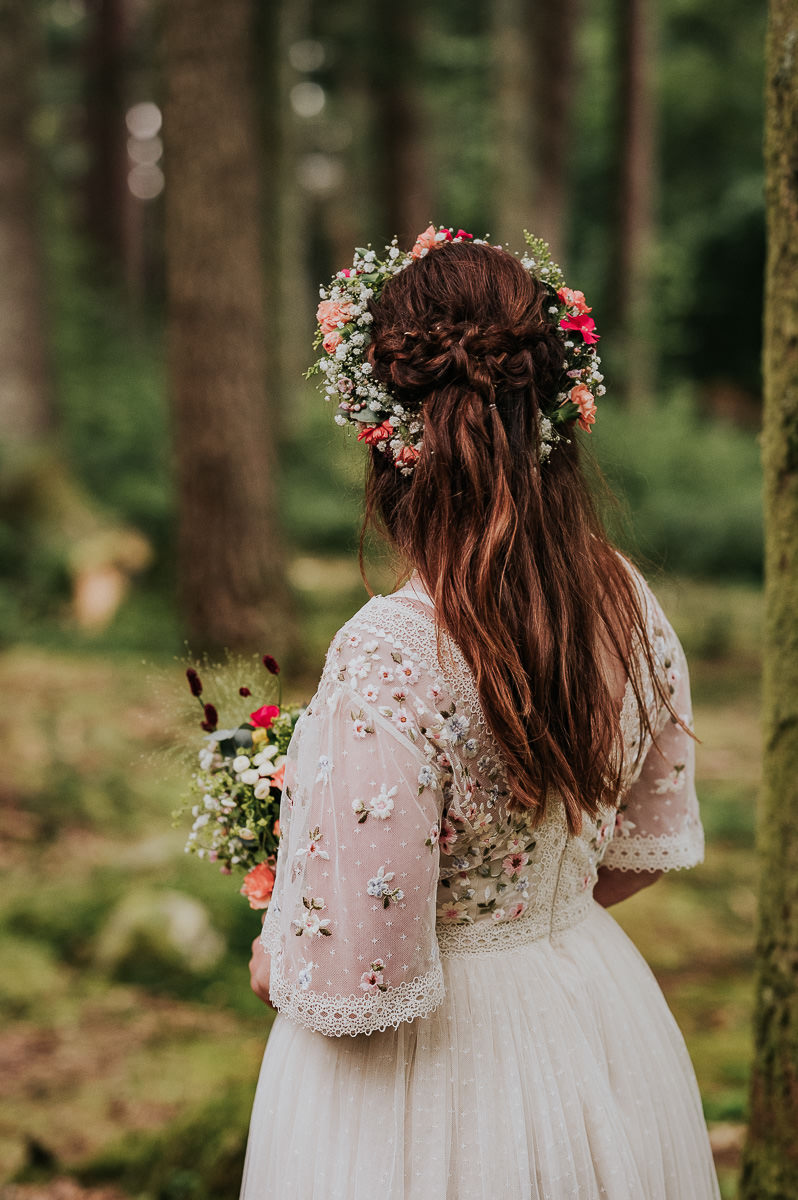 Nydelig brud med blomsterkrans i håret og en vakker kjole med broderte blomster på poserer i en skog i Haugesund på bryllupsdagen sin