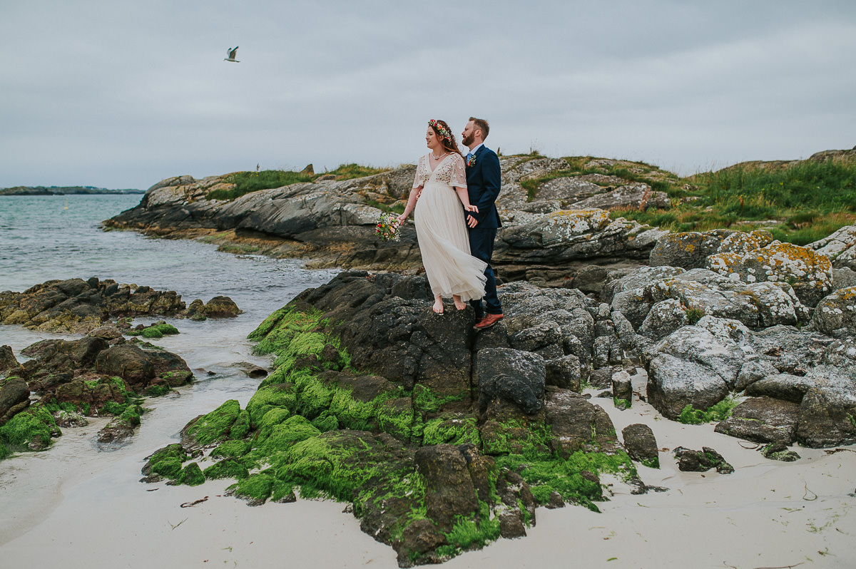 Utendørs sommer bryllup i Haugesund - brudeparet tar bilder på en vakker strand med turkis vann og bølger i bakgrunn