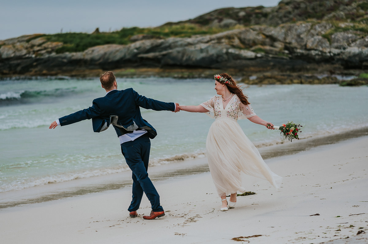 Utendørs sommer bryllup i Haugesund - brudeparet løper på en vakker strand med turkis vann og bølger i bakgrunn