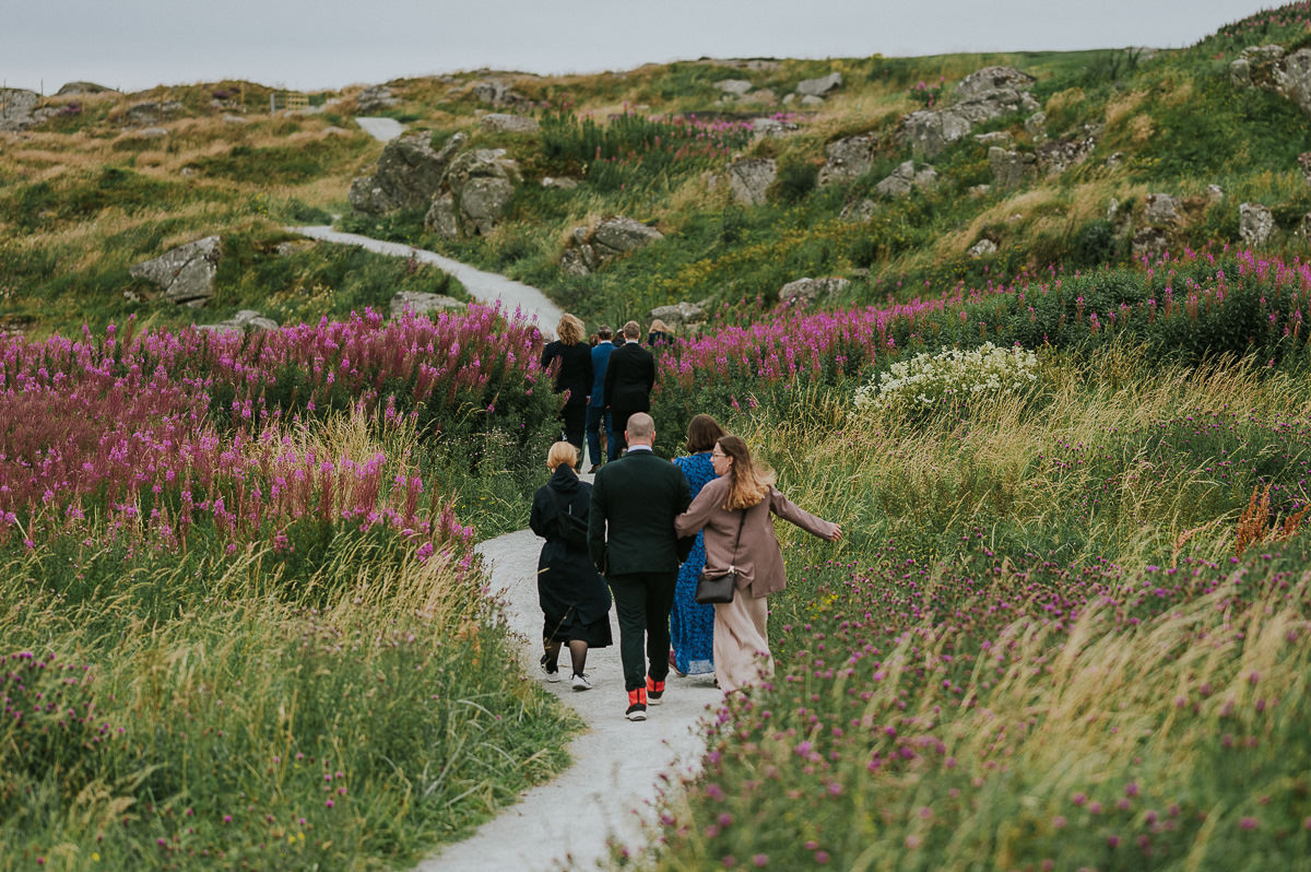 Bryllupsgjestene spaserer til vielsested på stranda i Haugesund - utendørs sommerbryllup på Vestlandet