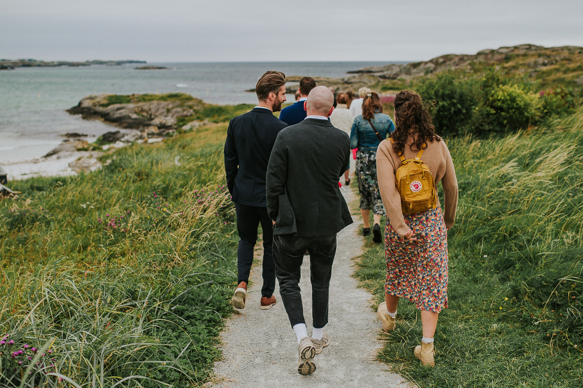 Bryllupsgjestene spaserer til vielsested på stranda i Haugesund - utendørs sommerbryllup på Vestlandet