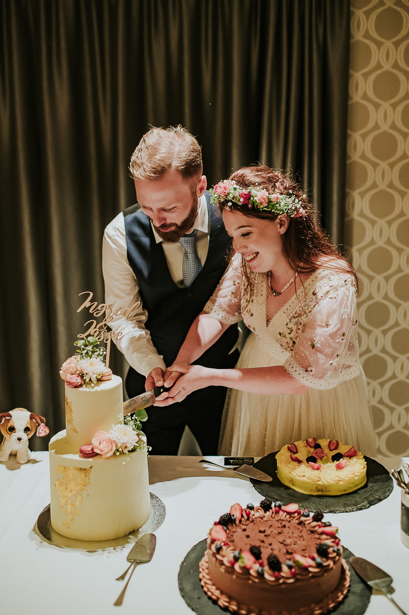 Brudeparet skjærer bryllupskake dekorert med blomster og makroner - sommerbryllup i Haugesund