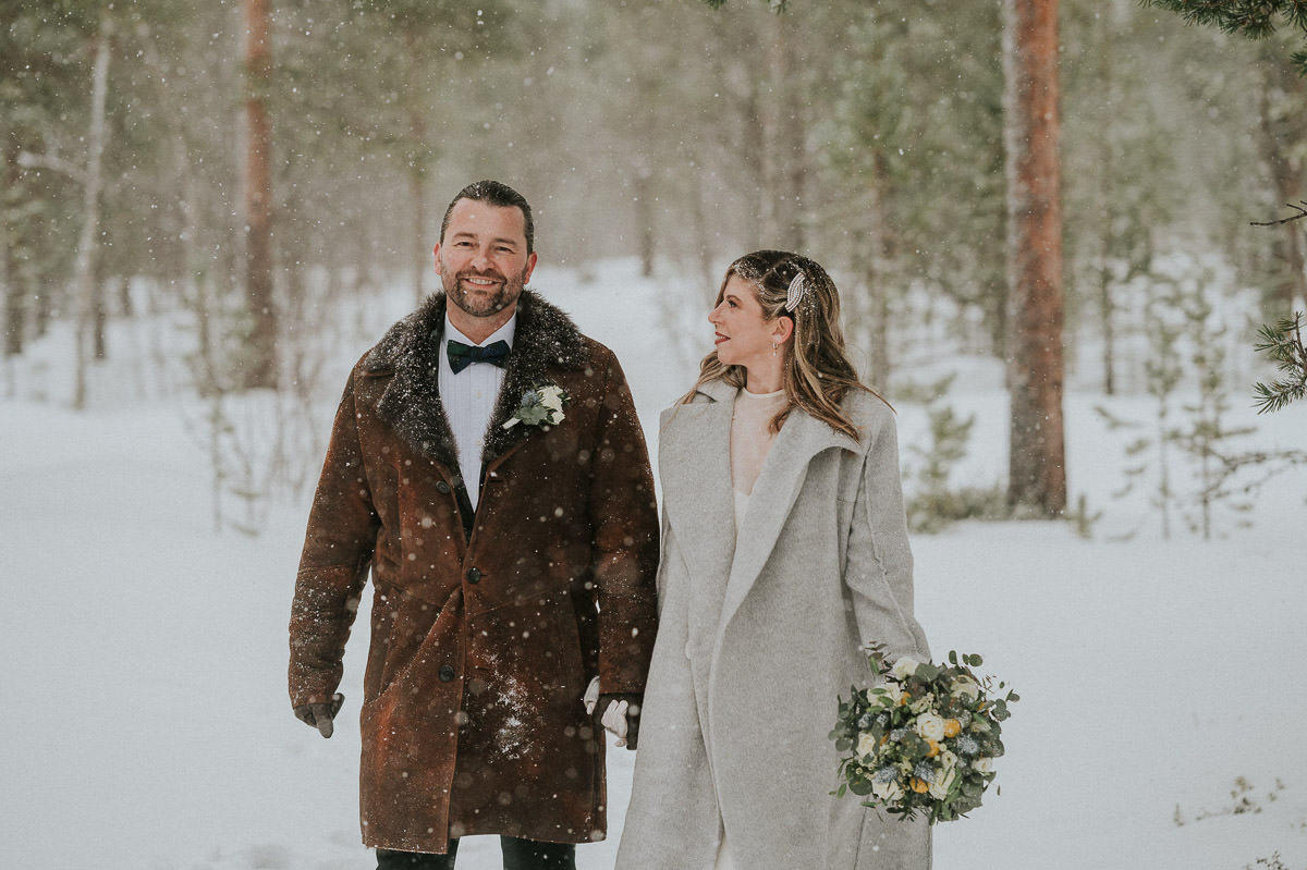 Bride and groom walking hand in hand under a heavy snowfall in a forest in Alta Norway on the day of their winter elopement