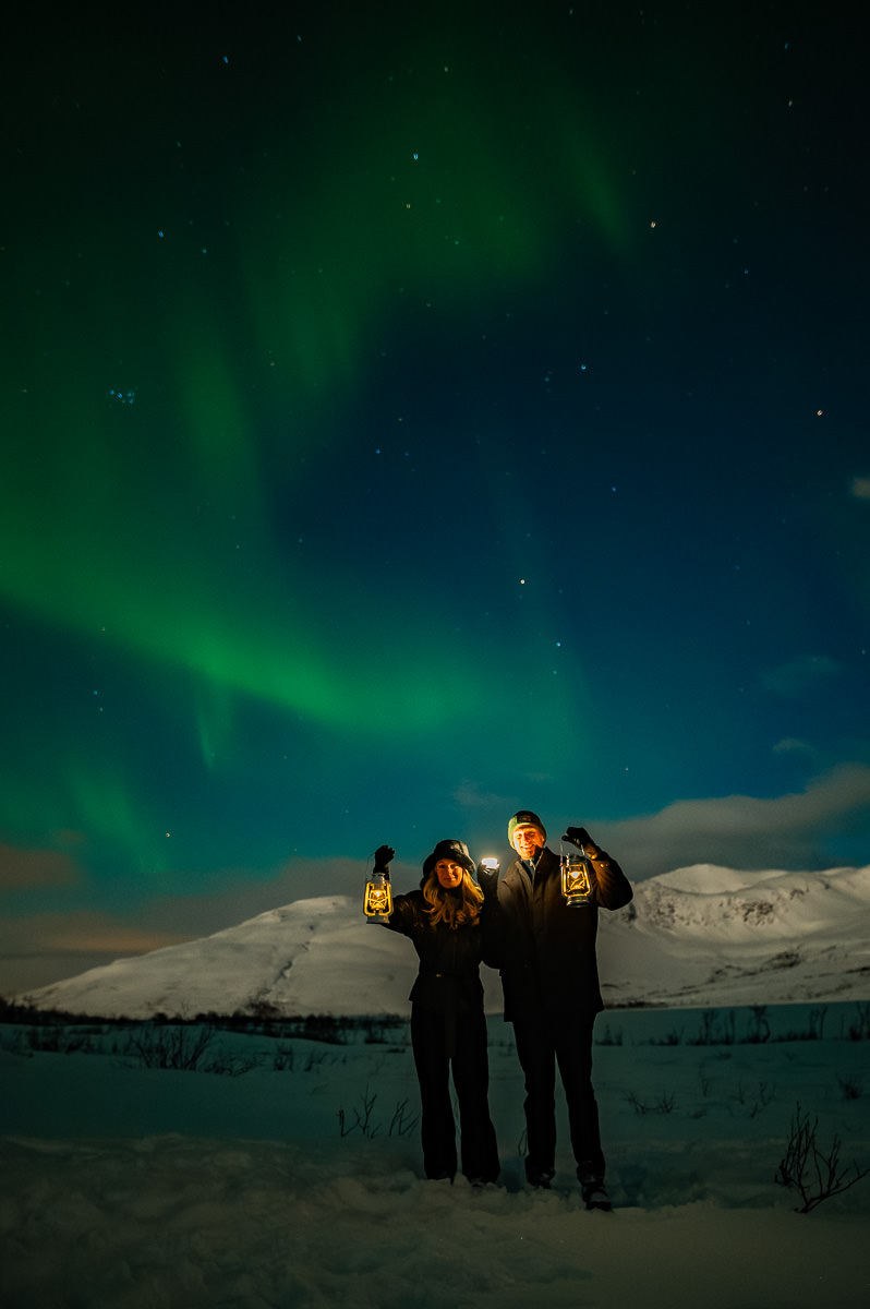 Cute couple standing under the arctic sky in Tromsø with dancing aurora borealis above them