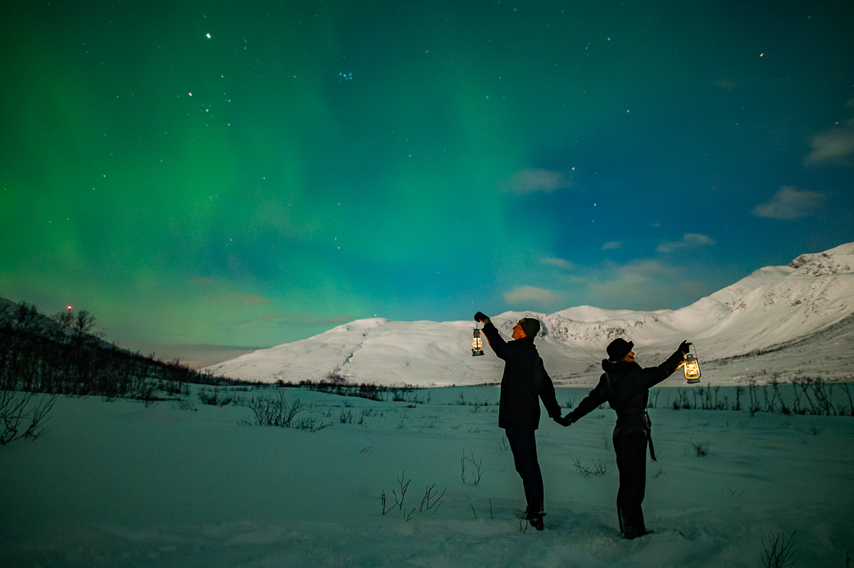 Surprise northern lights proposal in Tromsø Norway with aurora borealis dancing in the sky and snow-capped mountain landscape in the background
