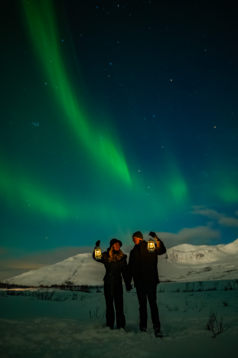 Cute couple standing under the arctic sky in Tromsø with dancing aurora borealis above them