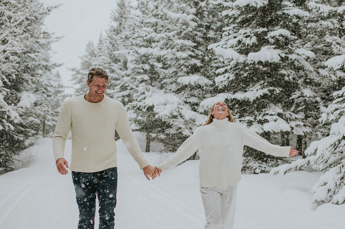 Cute couple running under a heavy snowfall in a forest in Tromsø on the day of their winter engagement photo session