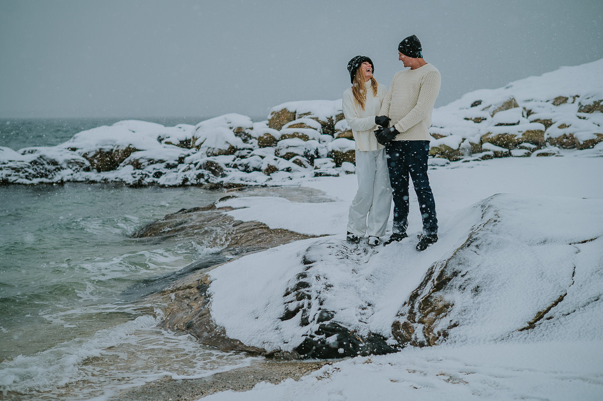 Cute couple cuddling by the sea under a beautiful snowfall in Tromsø Norway