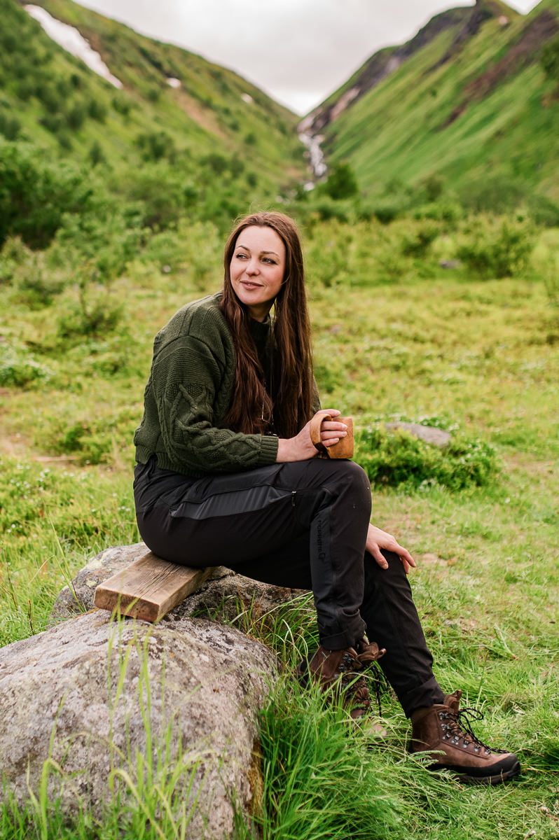 Tanja Skoglund - adventure photographer from Norway sitting with a cup of coffee in beautiful green mountain surroundings of Seiland National park in Norway 